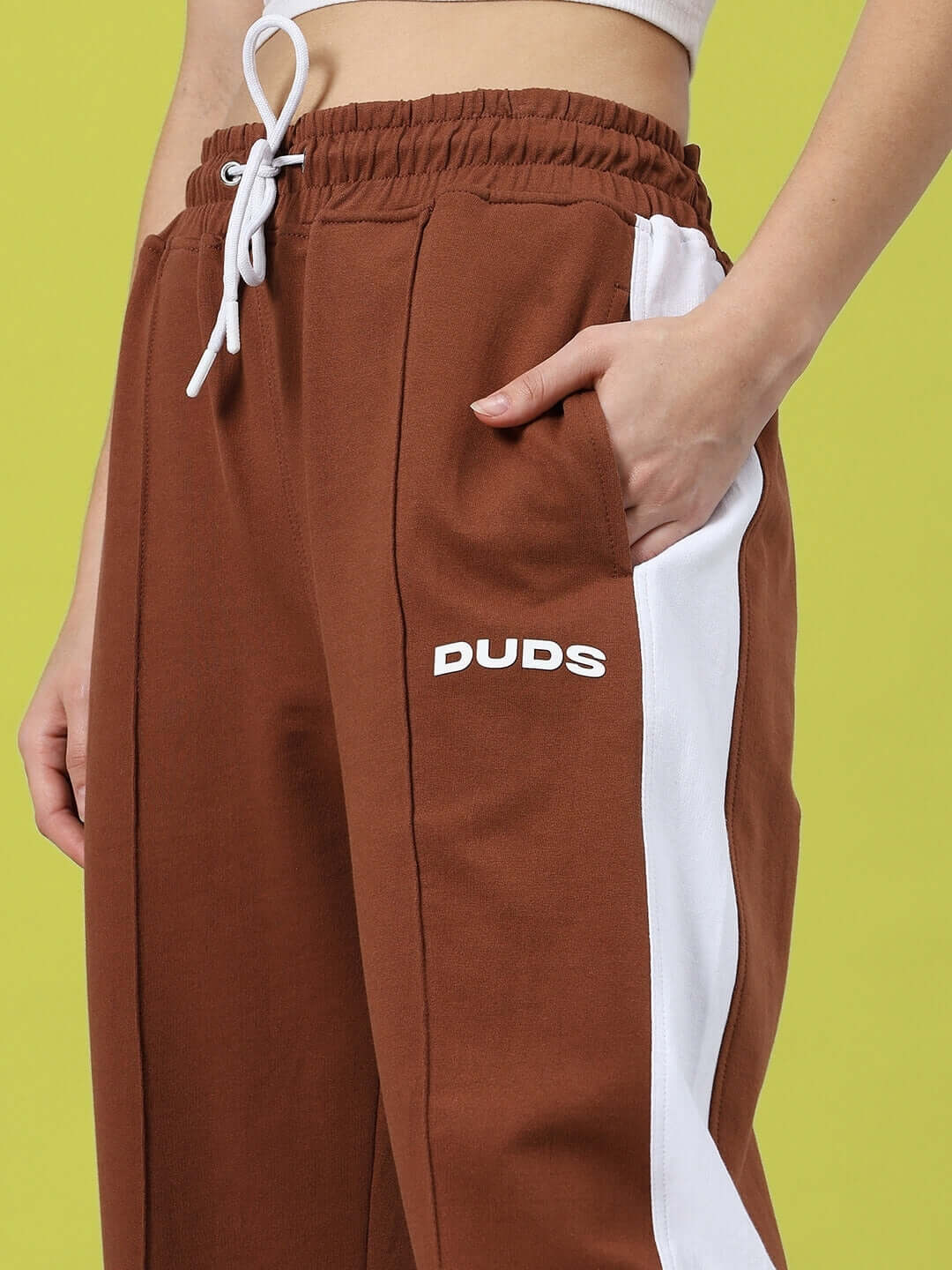Model wearing women's brown Wonder Slit Zipper Joggers by DUDS, featuring white stripes and elastic waist, ideal for custom fit.