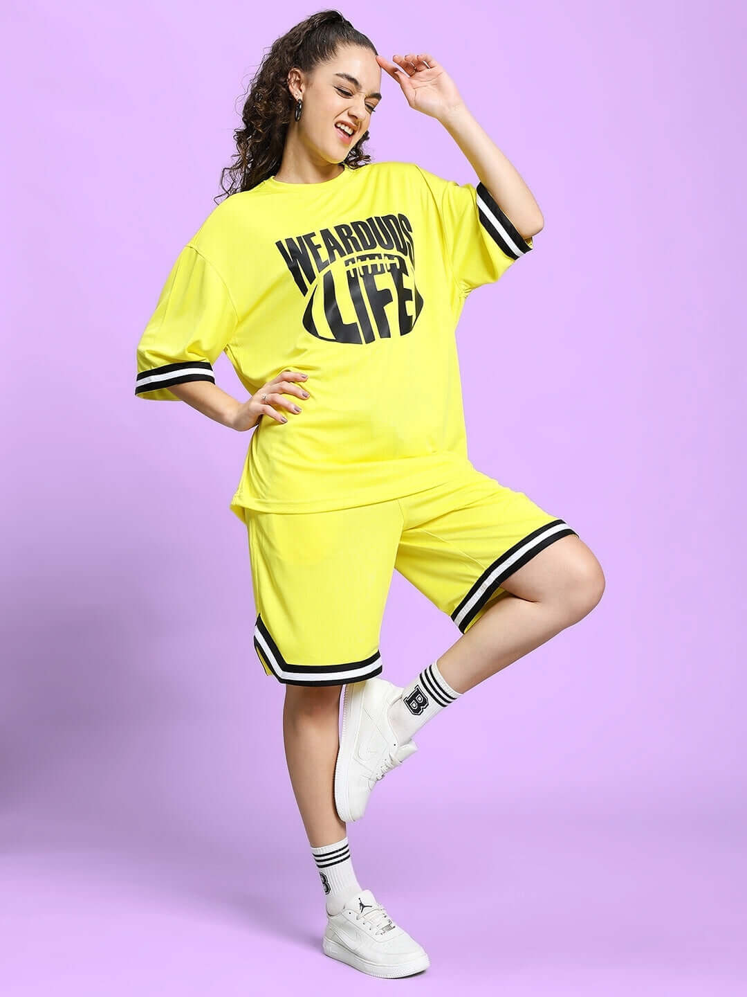 Woman wearing yellow colorblock co-ord set with 'Wear Your Life' lettering, sports polyester fabric, styled with white sneakers.