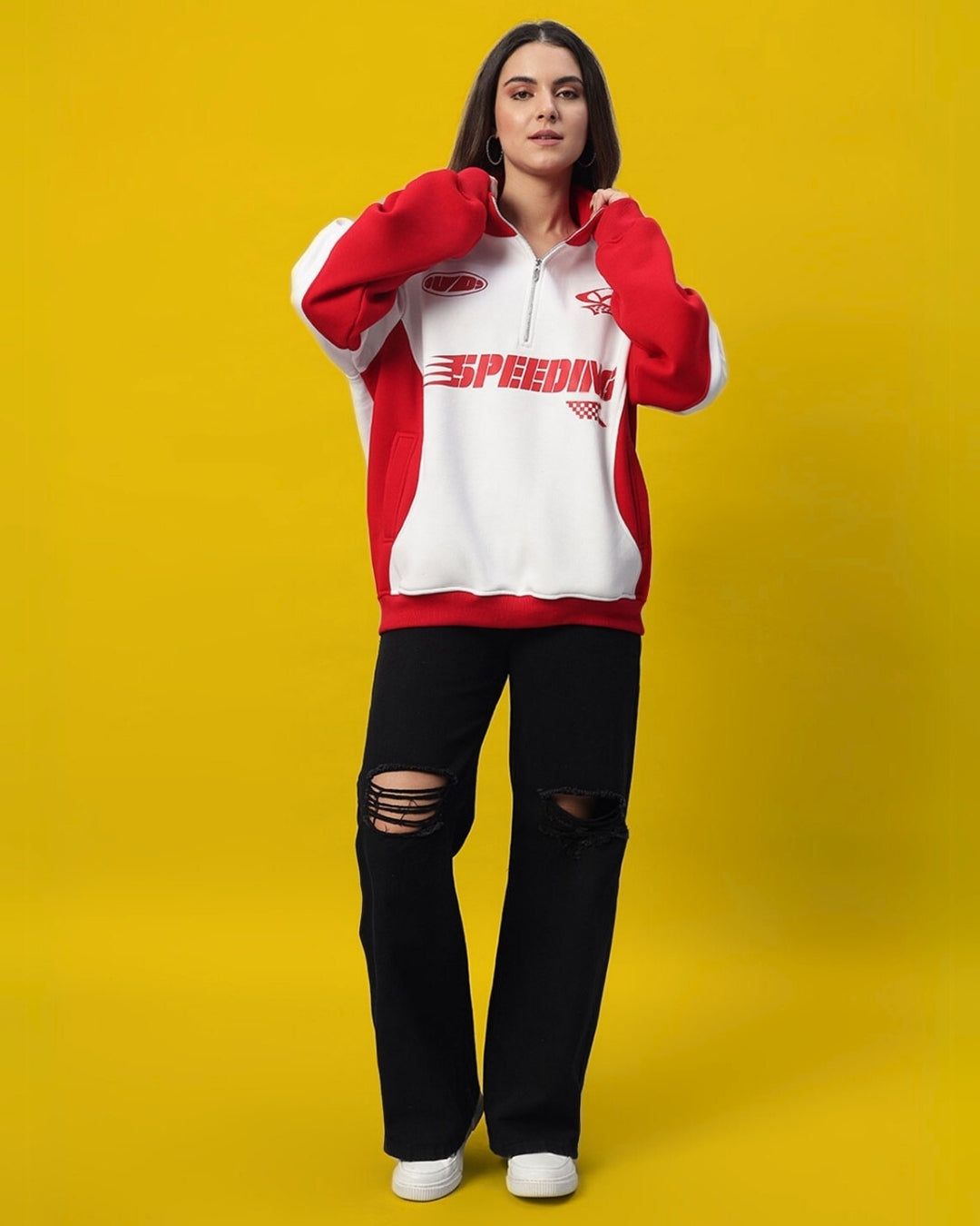 Woman wearing red and white colorblock jacket with 'SPEEDING' logo, paired with black ripped jeans on yellow background.