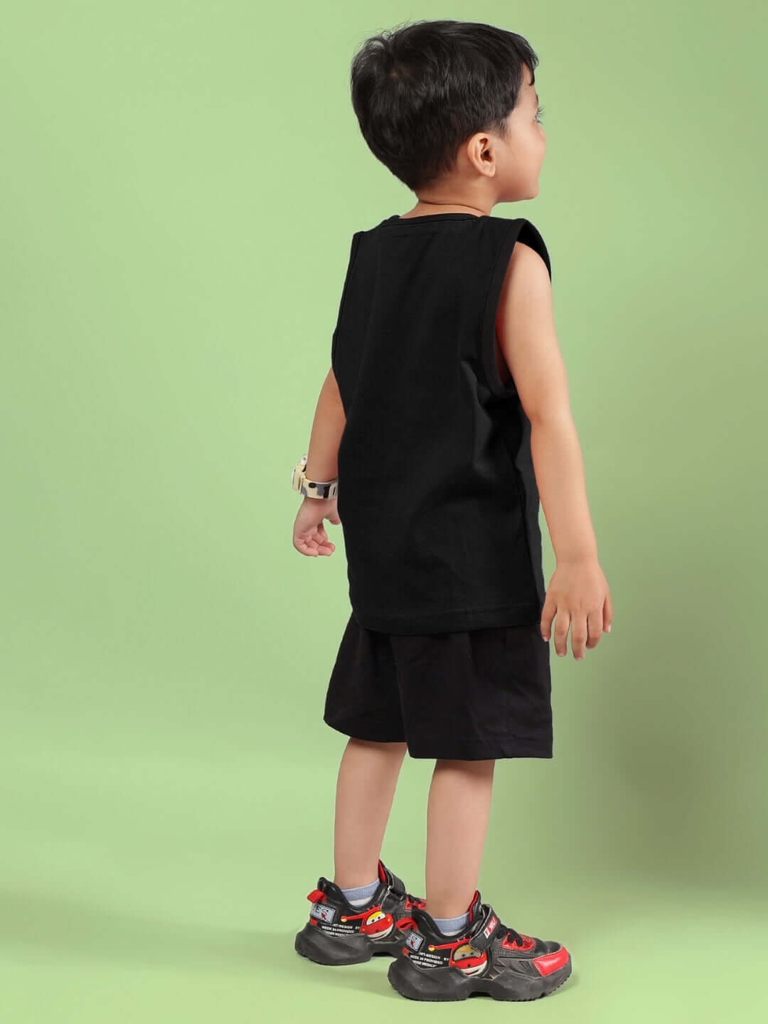 Child wearing AMIGA black co-ord set for boys and girls with shorts and sleeveless top, facing away with a mint green background.