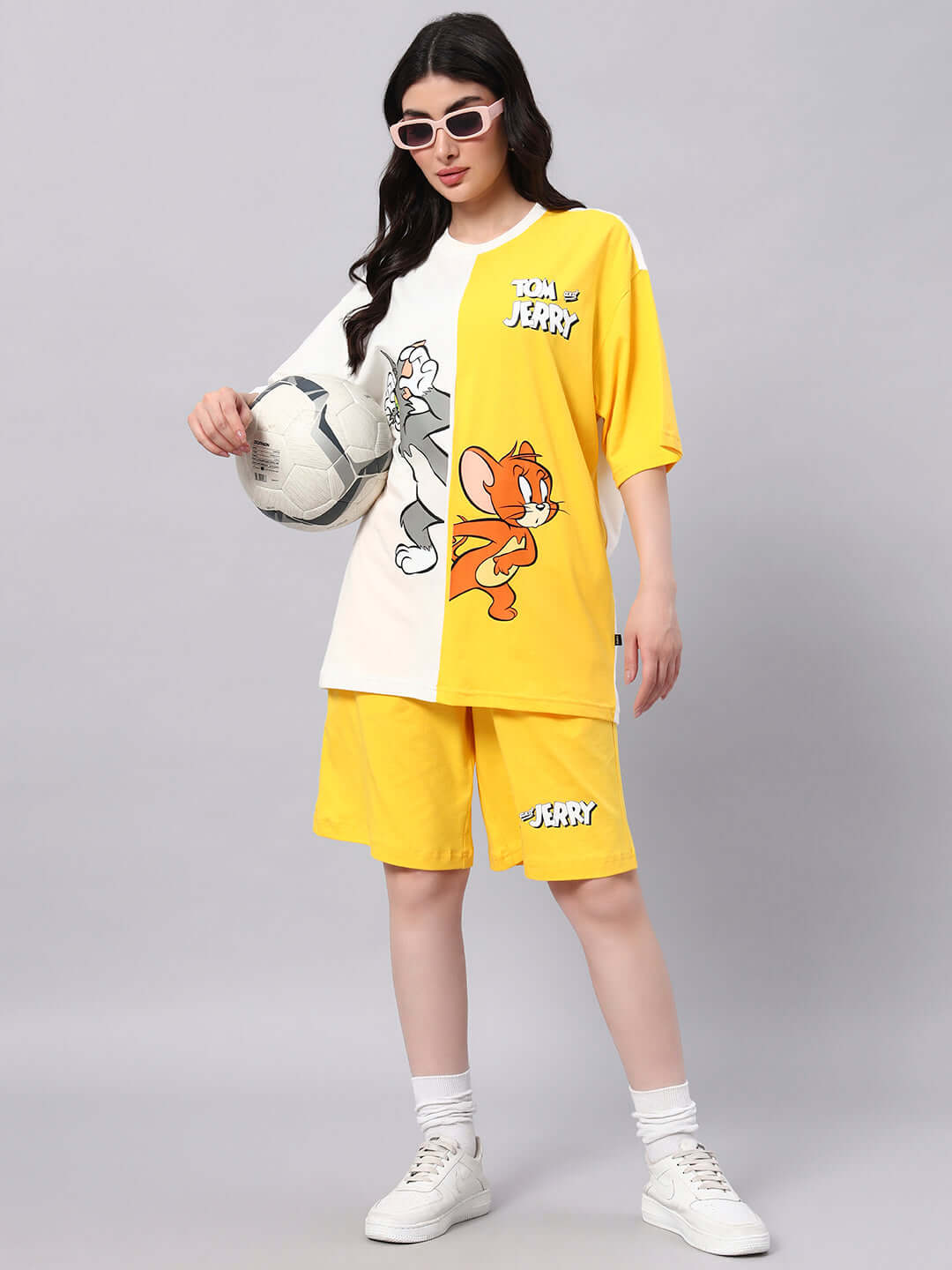 Fashion model wearing yellow Tom & Jerry shorts and matching top, holding a soccer ball, perfect for a casual summer look.