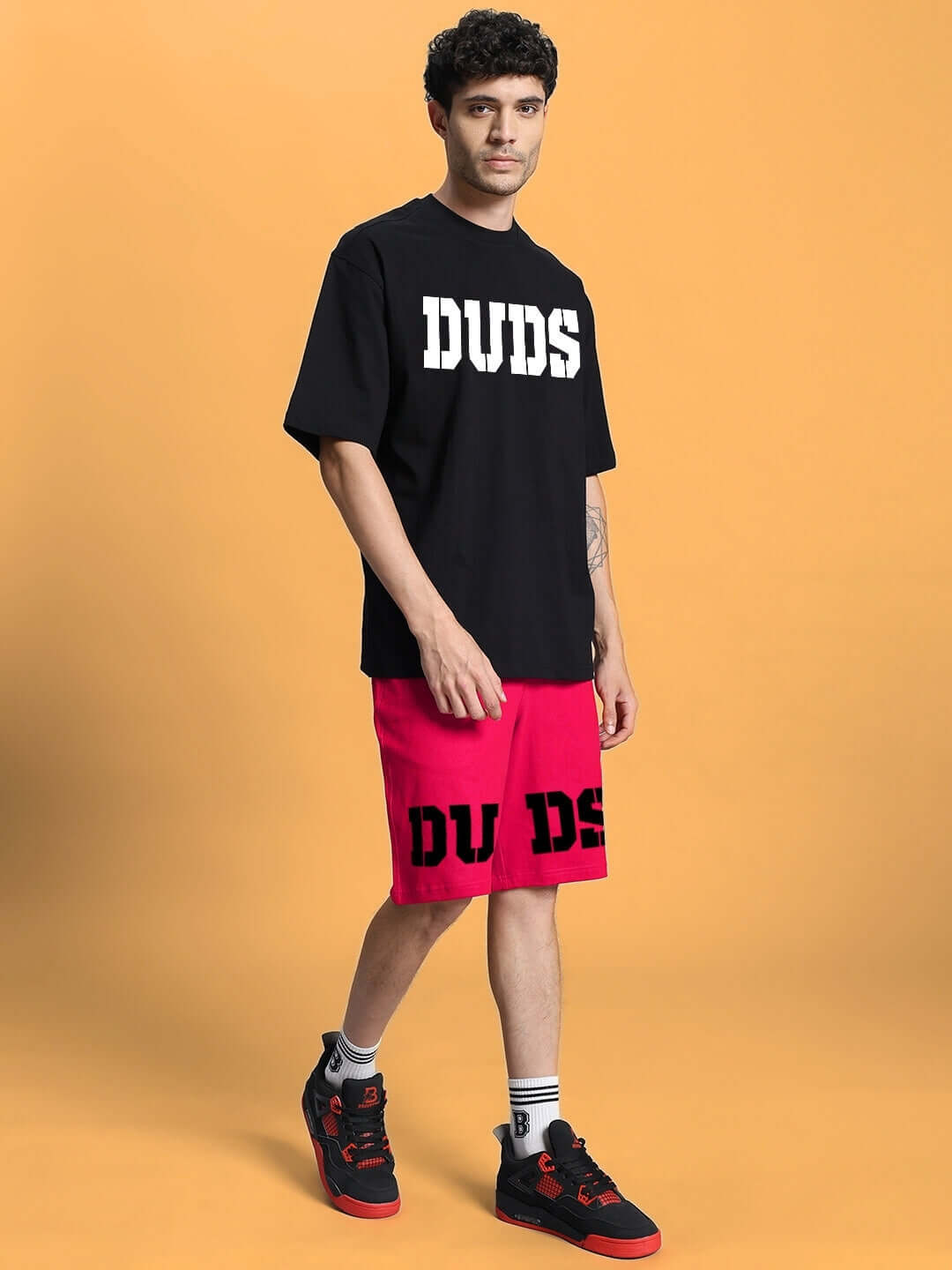 Model wearing DUDS Cherry Blossom Regular Fit Shorts in Pink, showcasing a casual style against a tan background.