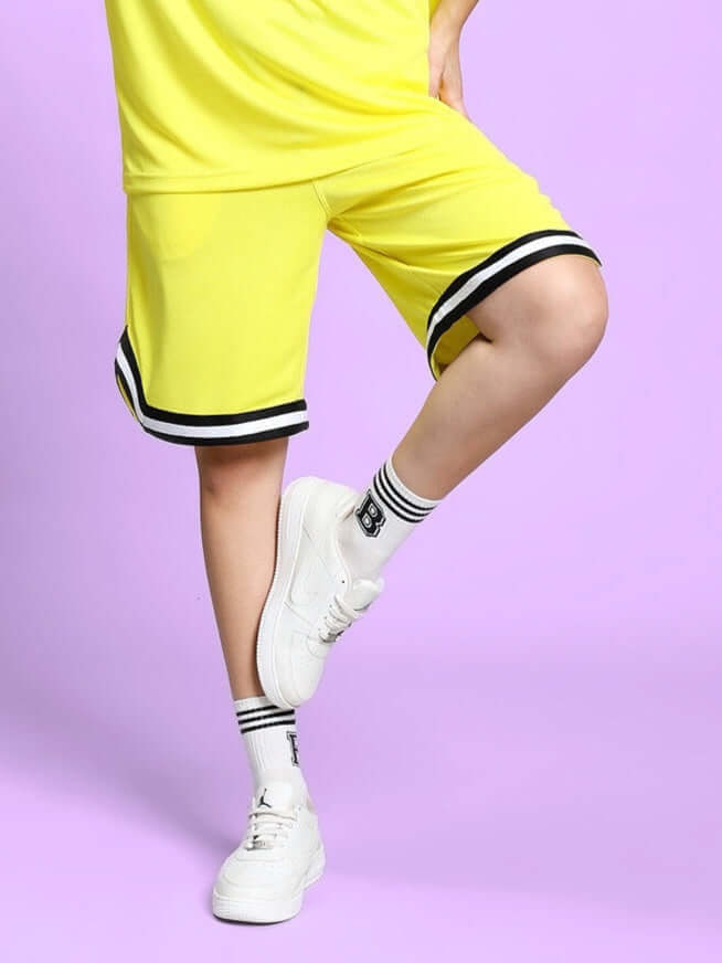 Yellow Women's Vigor Shorts with black trim, shown outdoors on lavender background, highlighting sporty design and regular fit.