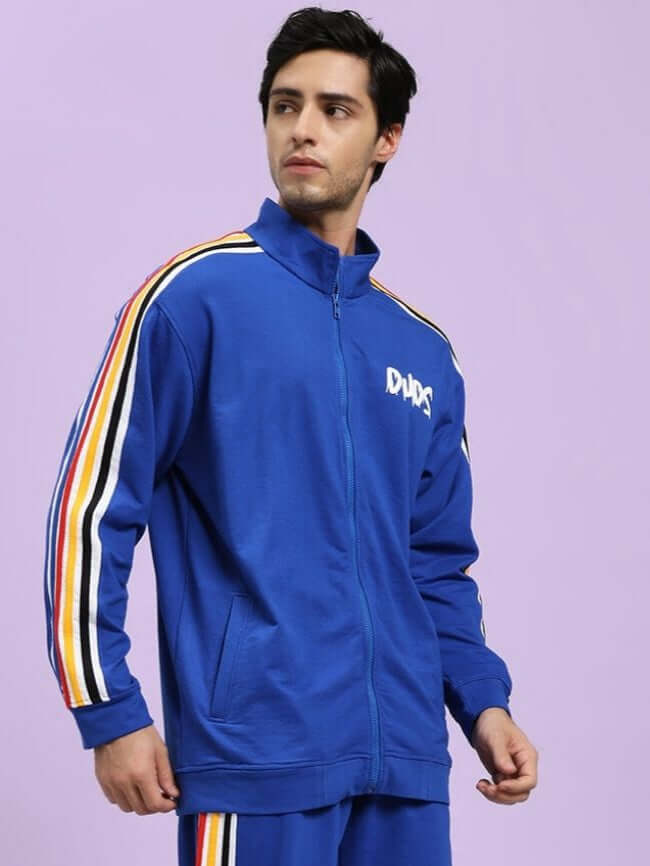 MODERN EDGE MULTI-STRIPE JACKET ROYAL BLUE Man wearing a blue tracksuit with colorful stripes on a light purple background