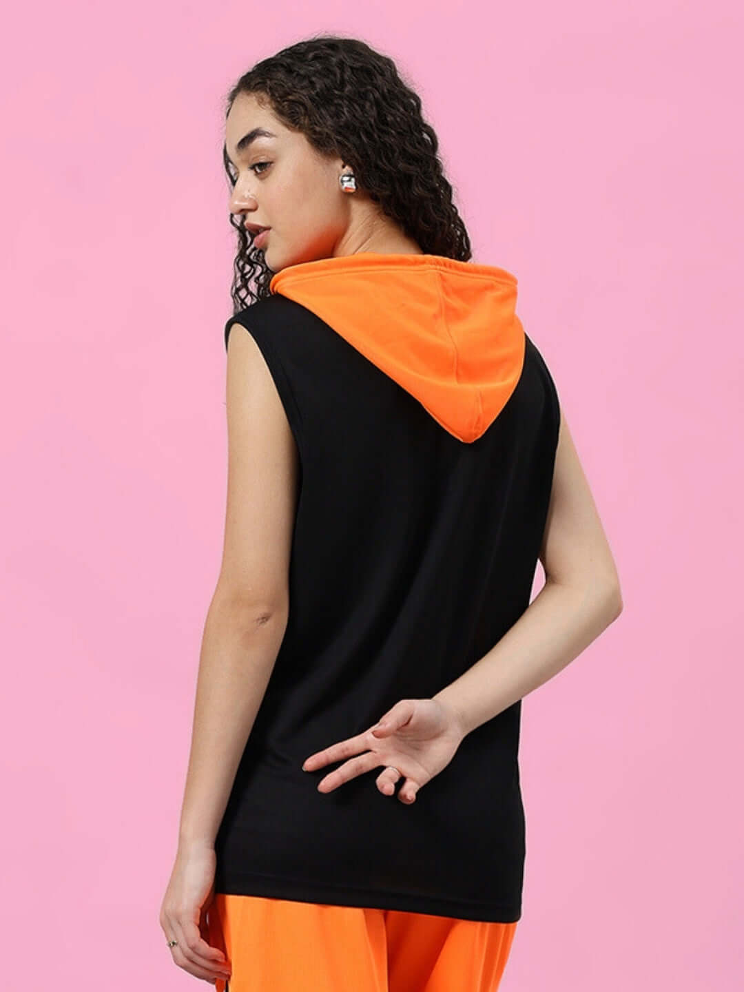 Woman wearing Women's Franky Gym T-Shirt in orange and black, back view, sleeveless design against a pink background.