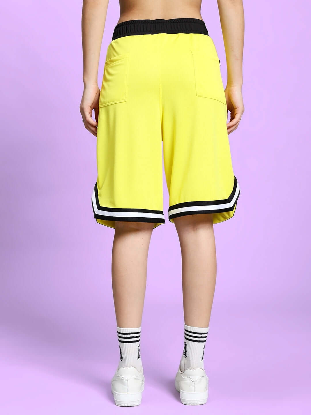 Back view of women's yellow Vigor regular fit shorts with black waistband and striped hem, showcasing casual sporty style.