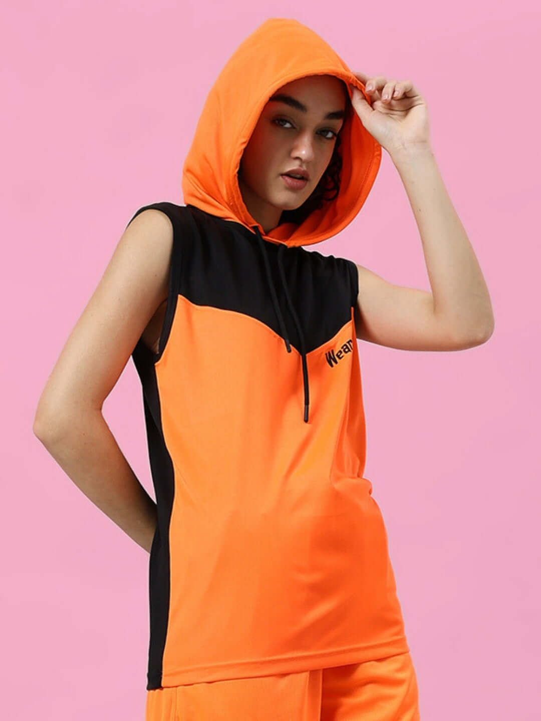 Model wearing orange and black women's Franky gym T-shirt with hood on pink background.
