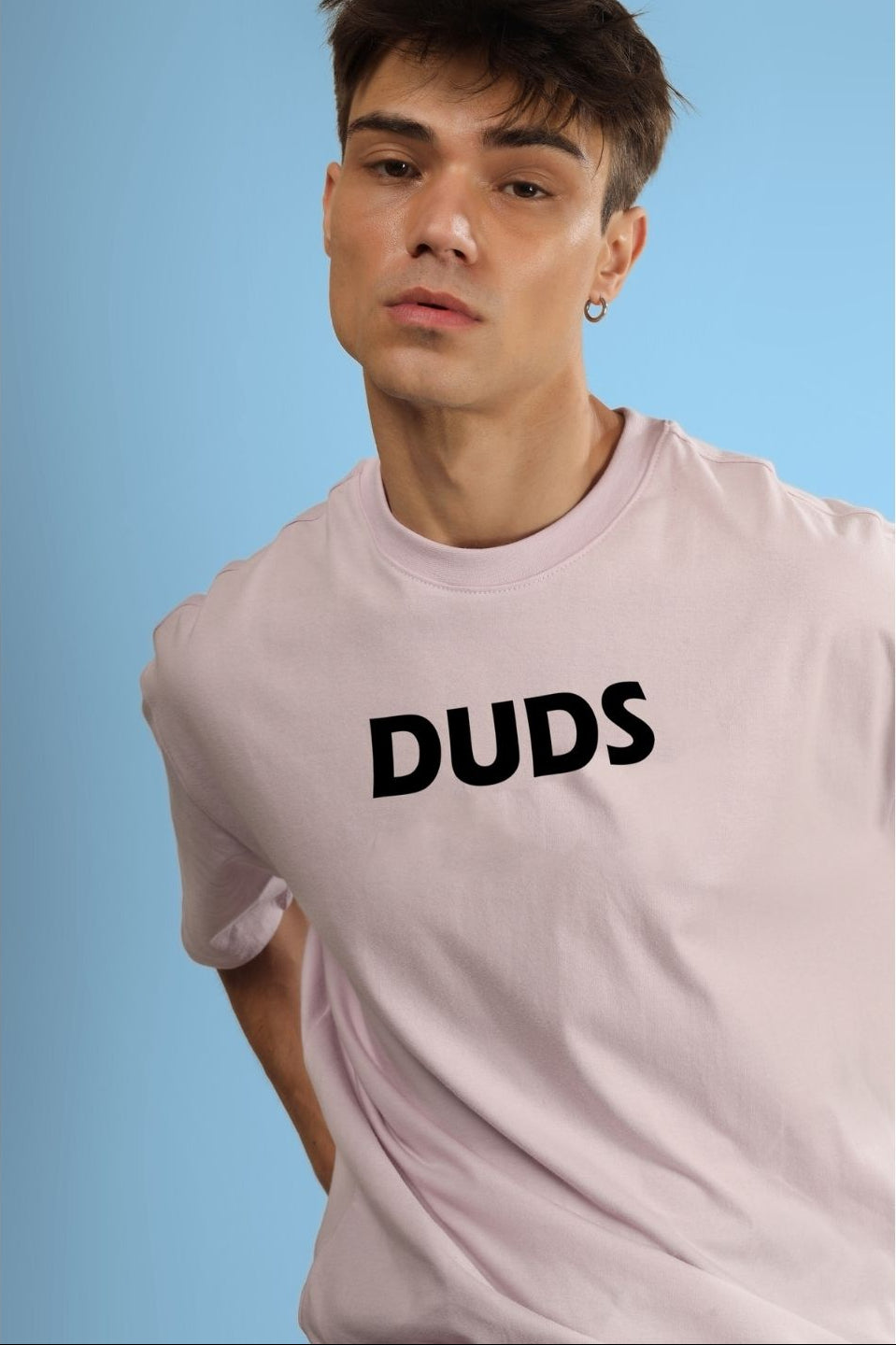 Man wearing a pink t-shirt with 'DUDS' printed on the front, posing against a blue background.
