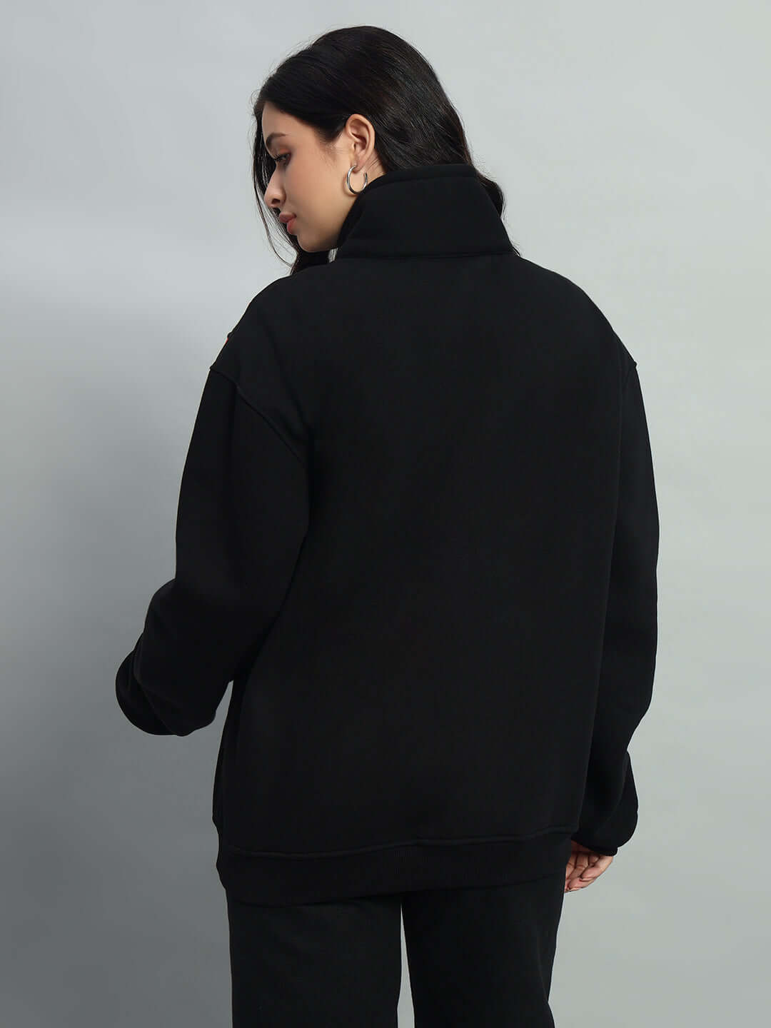 Woman wearing black crossbar fleece colorblock jacket, back view, showcasing high collar and relaxed fit.