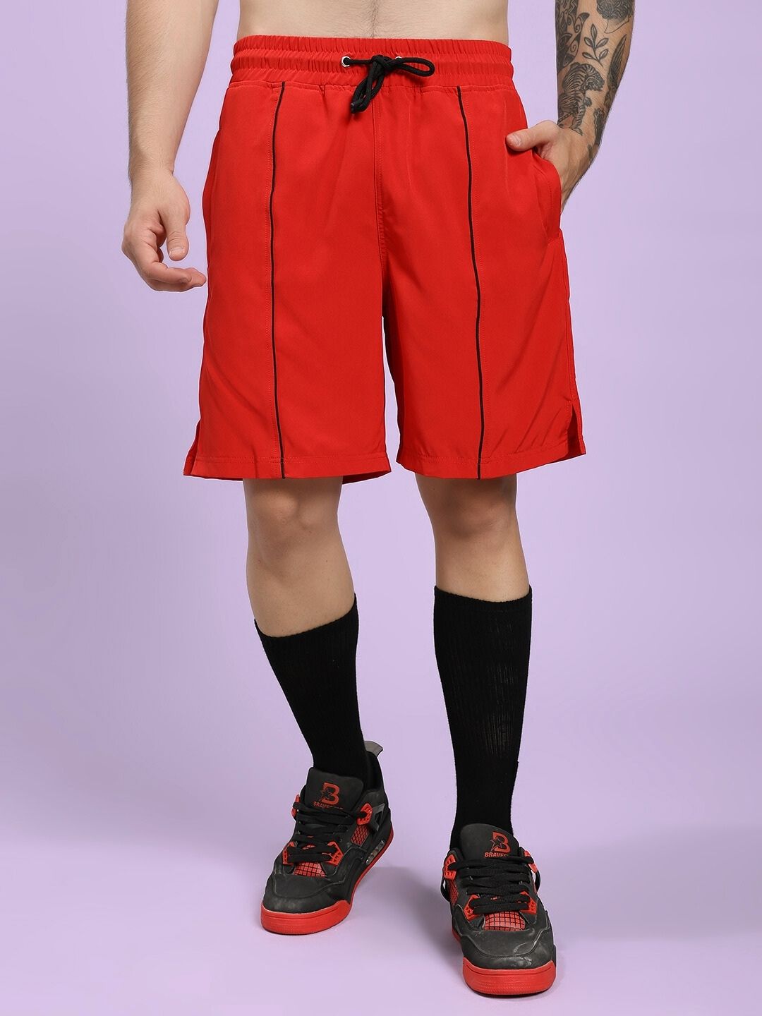 Person wearing red shorts with black drawstring and piping on a light purple background