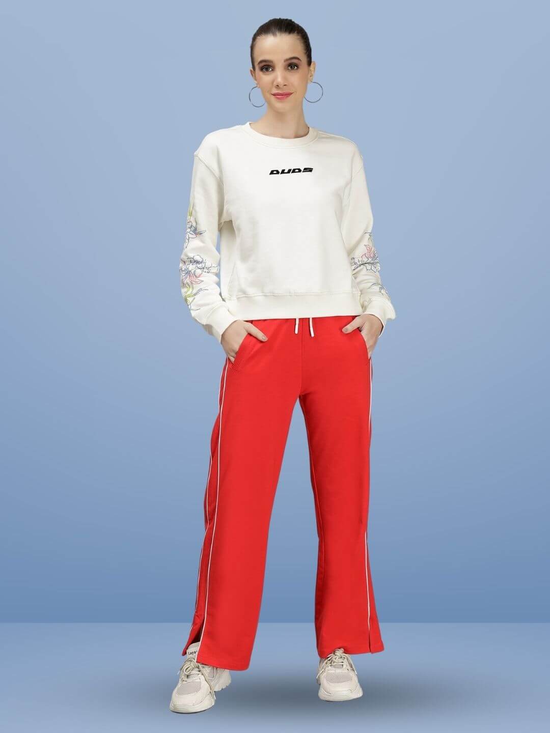 Model wearing WEARDUDS RIO RELAXED FIT JOGGERS RED with white piping, handmade by DUDS, showcasing a casual sporty outfit against a blue background.
