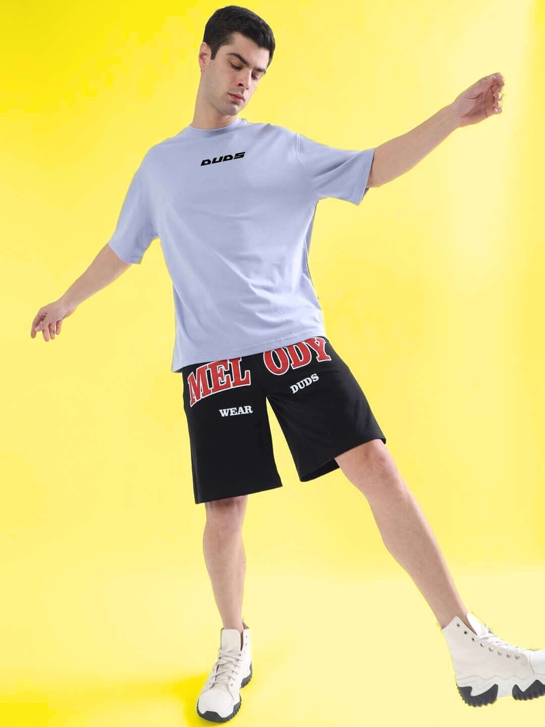 Person wearing FIND YOUR WAY OVER-SIZED T-SHIRT LILAC with printed shorts, standing against a yellow background.