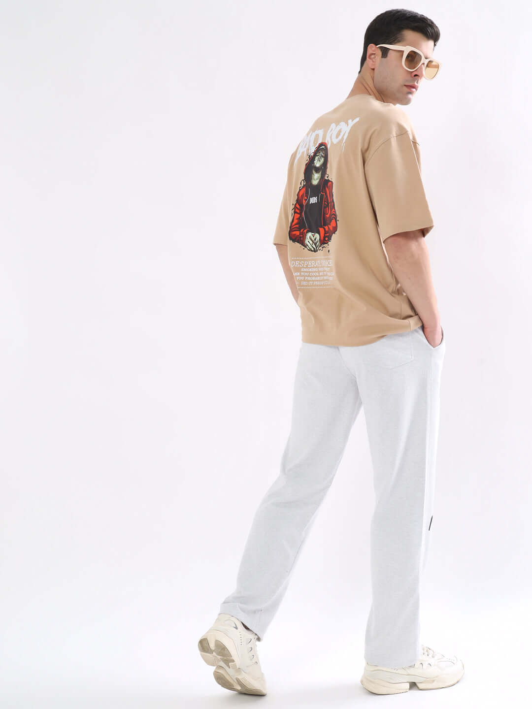 Man wearing BAD BOY OVER-SIZED T-SHIRT NUDE with graphic print, side view, paired with white pants and sunglasses, fashion style.