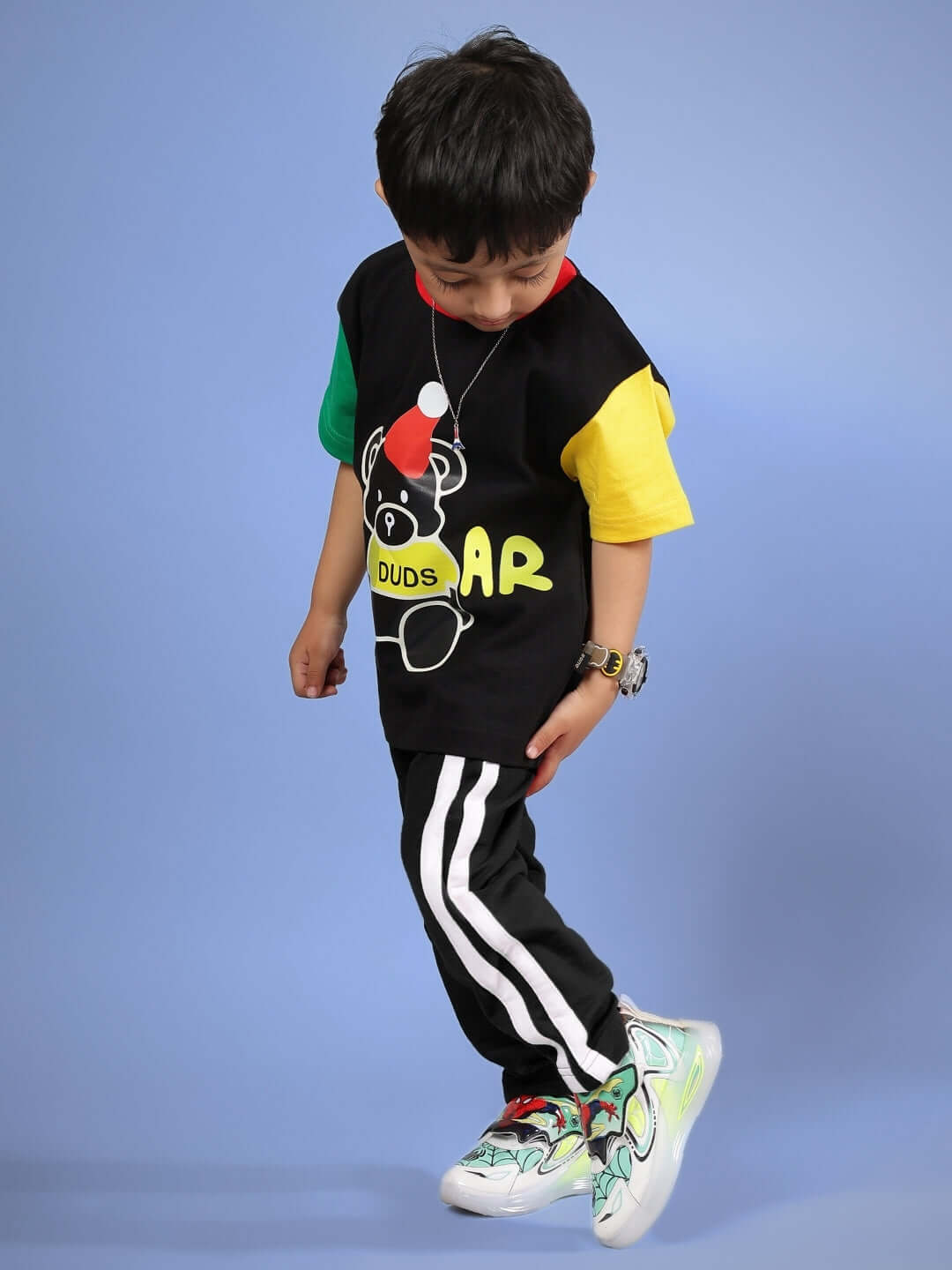 Child wearing colorful black DUDS MOCHA co-ord set, featuring a playful bear design, suitable for boys and girls, against a blue background.