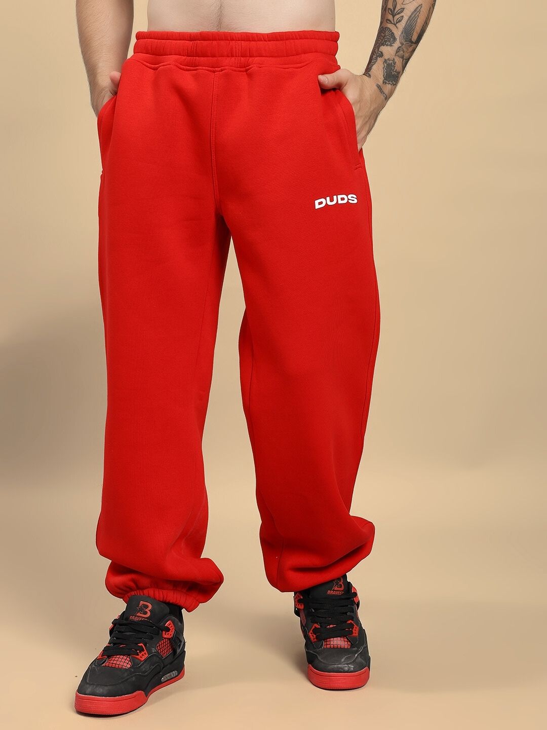 Red sweatpants with 'DUDE' logo worn by a person on a beige background