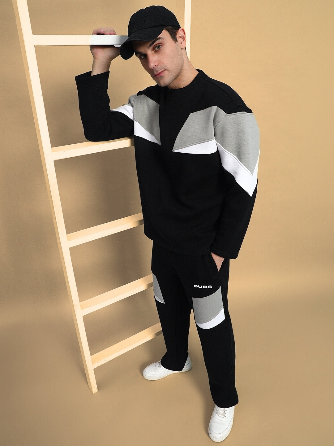 Model wearing Aviator Colorblock Co-Ord in black with grey and white accents, standing by a wooden ladder, showcasing modern fashion style.