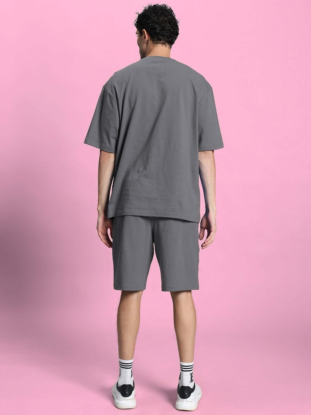 Back view of grey summer co-ord shorts set made from premium cotton French terry, worn by a male model against a pink background.