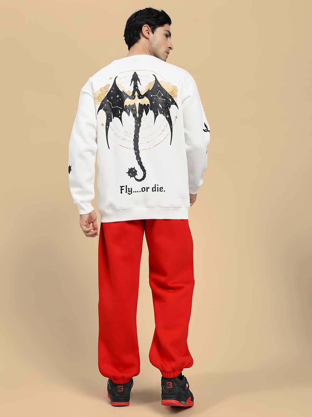 Person wearing a white sweatshirt with a dragon design and red pants on a beige background