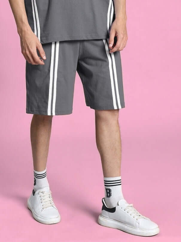 Model wearing grey Outlook regular fit shorts with white stripes, paired with white sneakers and socks, set against a pink background.
