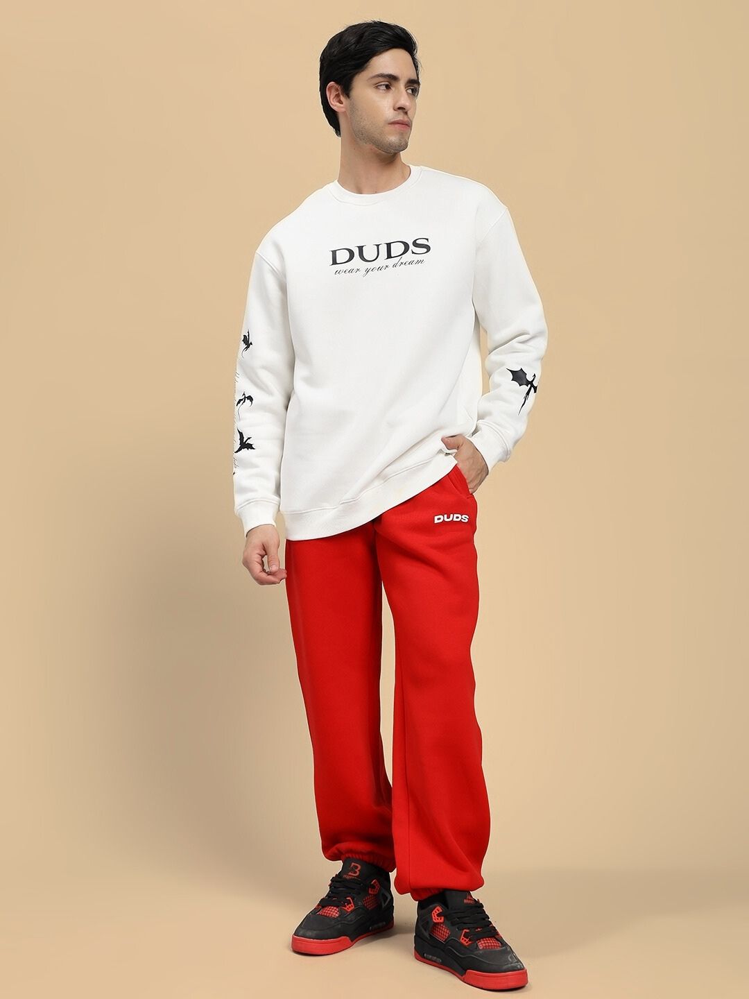 Person wearing a white sweatshirt with 'DUDS' branding and red pants on a beige background