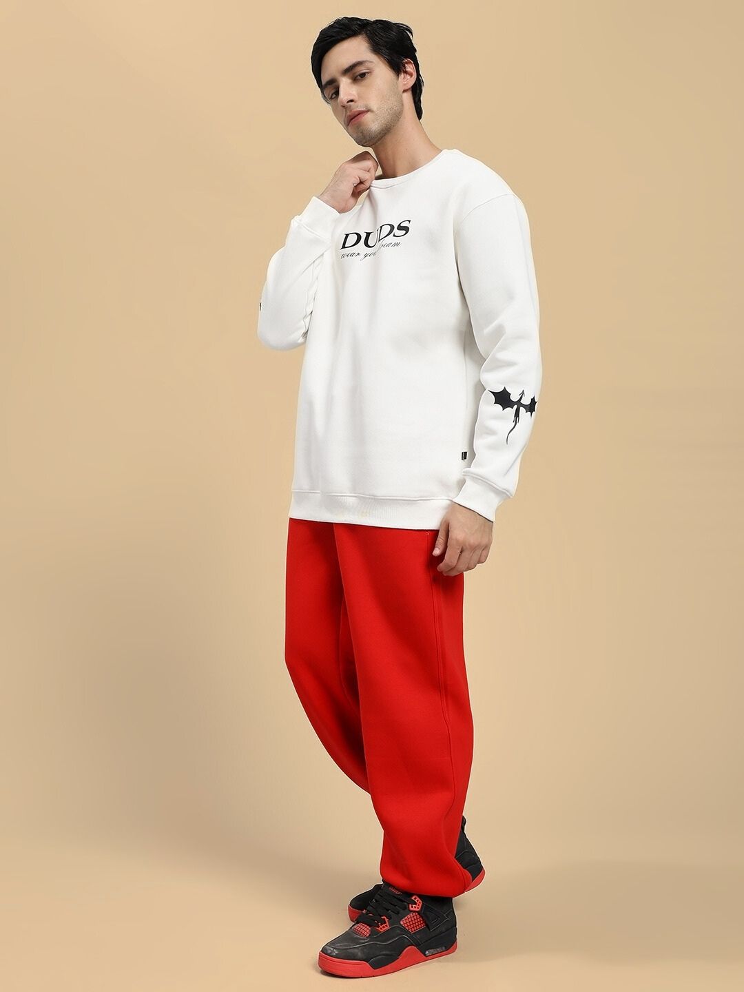 Person wearing a white hoodie with branding and red pants on a beige background