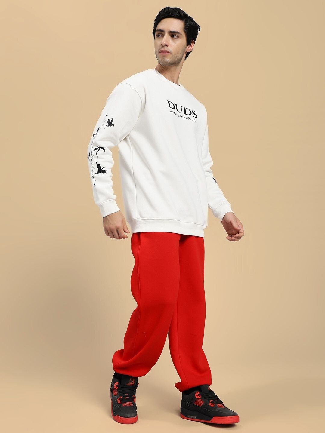 Man wearing a white sweatshirt with 'DUDE' text and red pants on a beige background