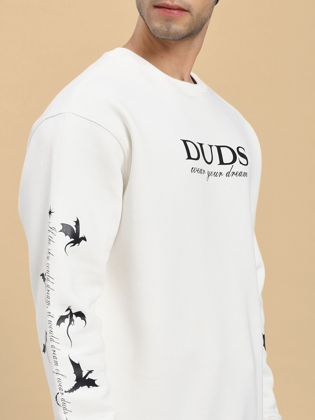 White sweatshirt with dragon designs and text on sleeves, worn by a person against a beige background.
