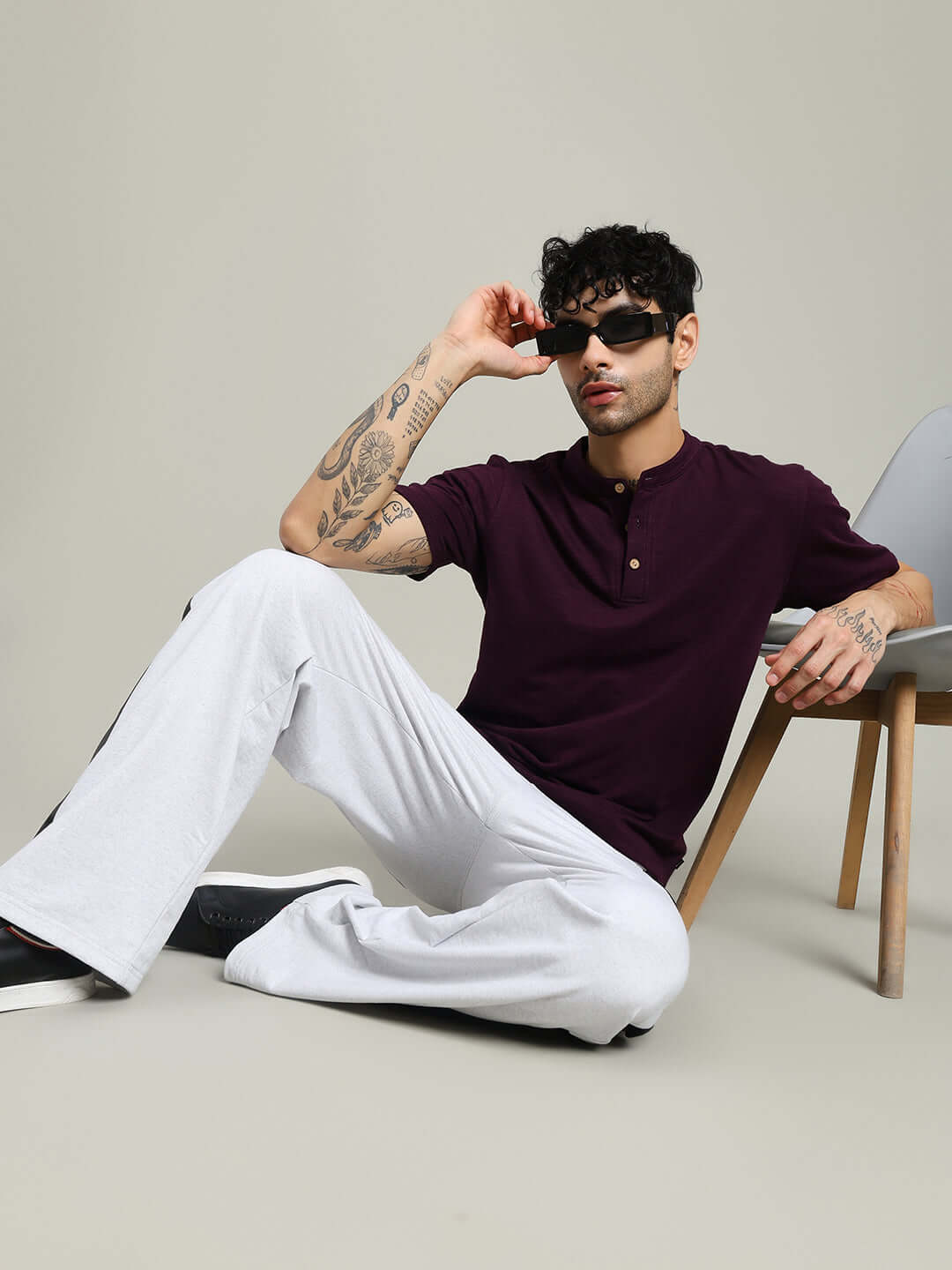 Man wearing Albet Regular Fit Purple T-Shirt and white pants, sitting casually on the floor, showcasing fashion-forward style.