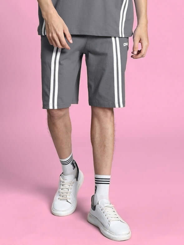 Person wearing grey Outlook Regular Fit Shorts with white stripes, showcasing comfortable casual style on a pink background.