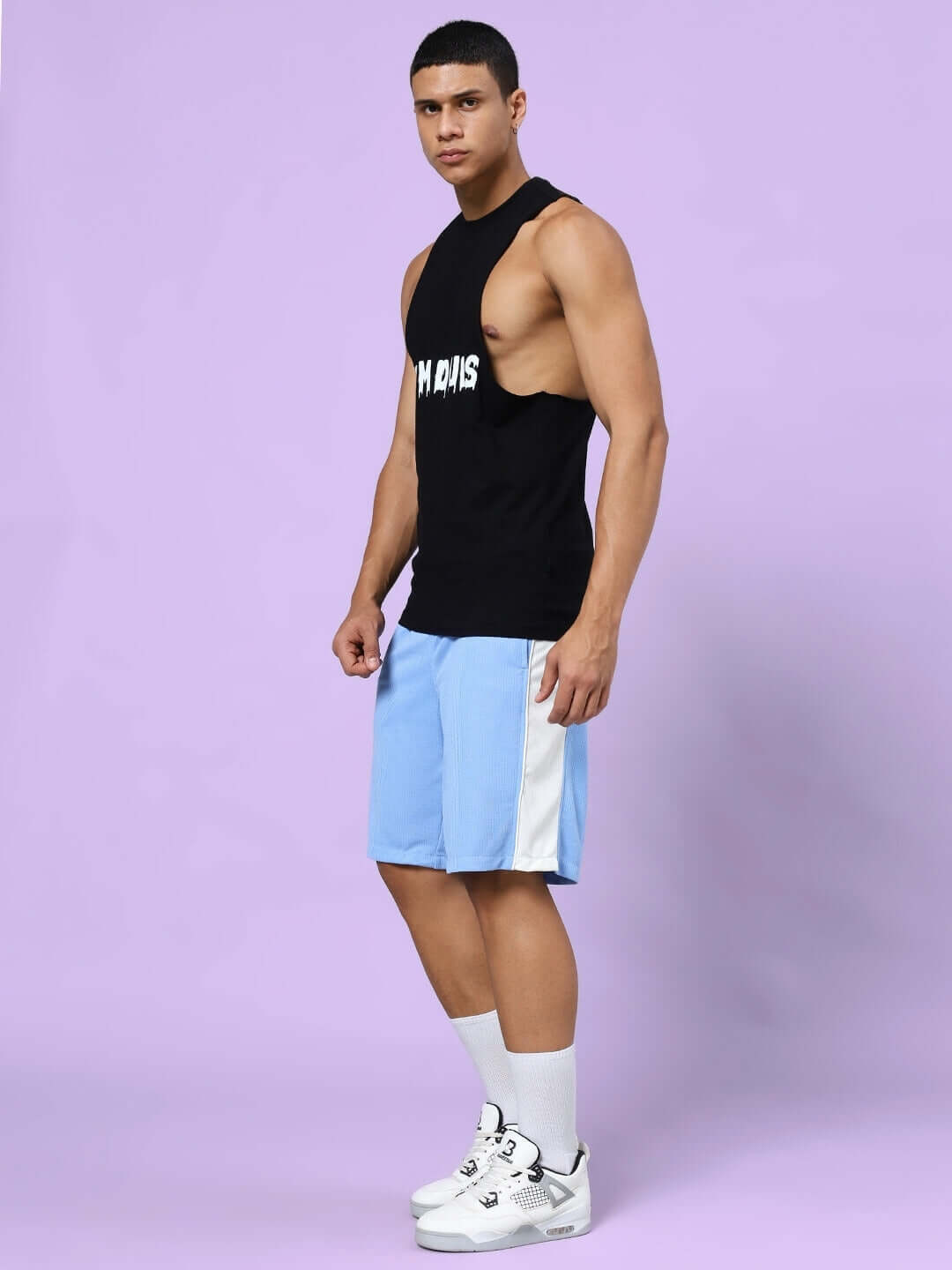 Man wearing CRUNCH GYM CO-ORD SET in black and blue, featuring a sleeveless black T-shirt and blue shorts, standing against a purple background.