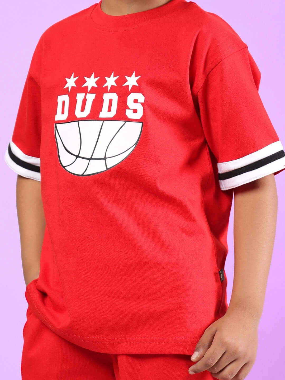 Child wearing red oversized t-shirt with DUDS logo, featuring basketball design and star details, suitable for boys and girls.