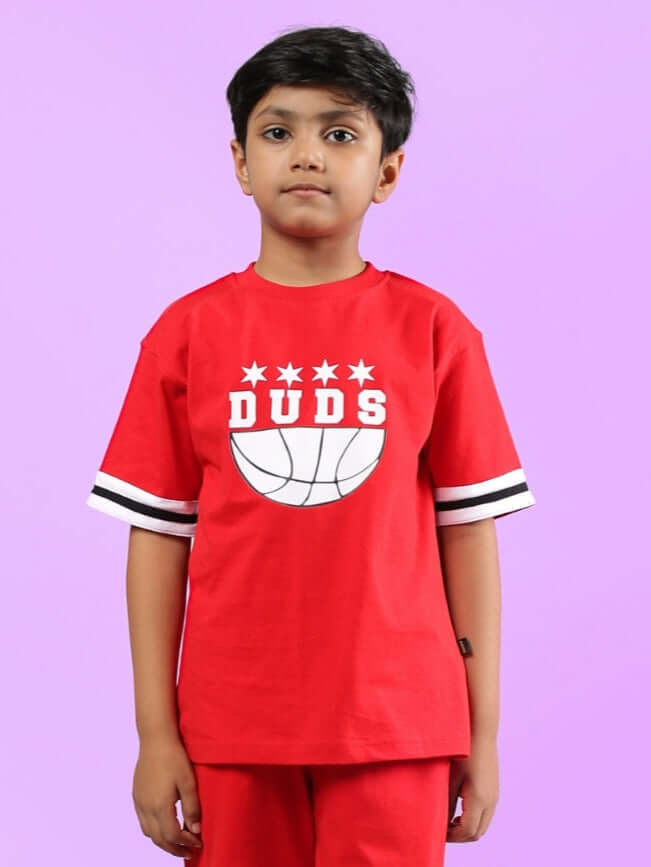 Child wearing a red Diggin oversized t-shirt for boys and girls with a basketball logo by DUDS, against a purple background.