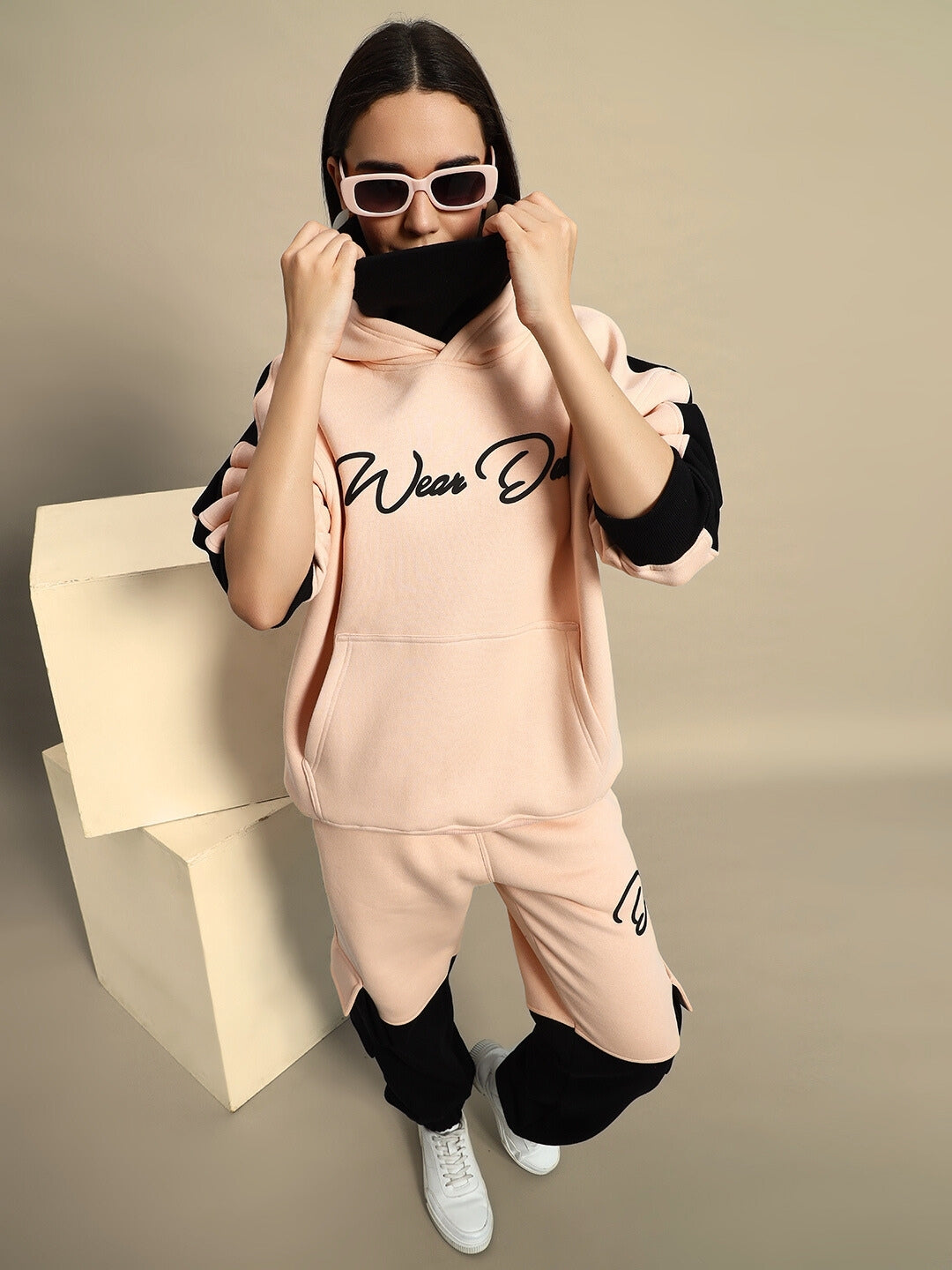 Woman modeling beige-black fleece hoodie with sunglasses, showcasing stylish women's regiment fashion look.
