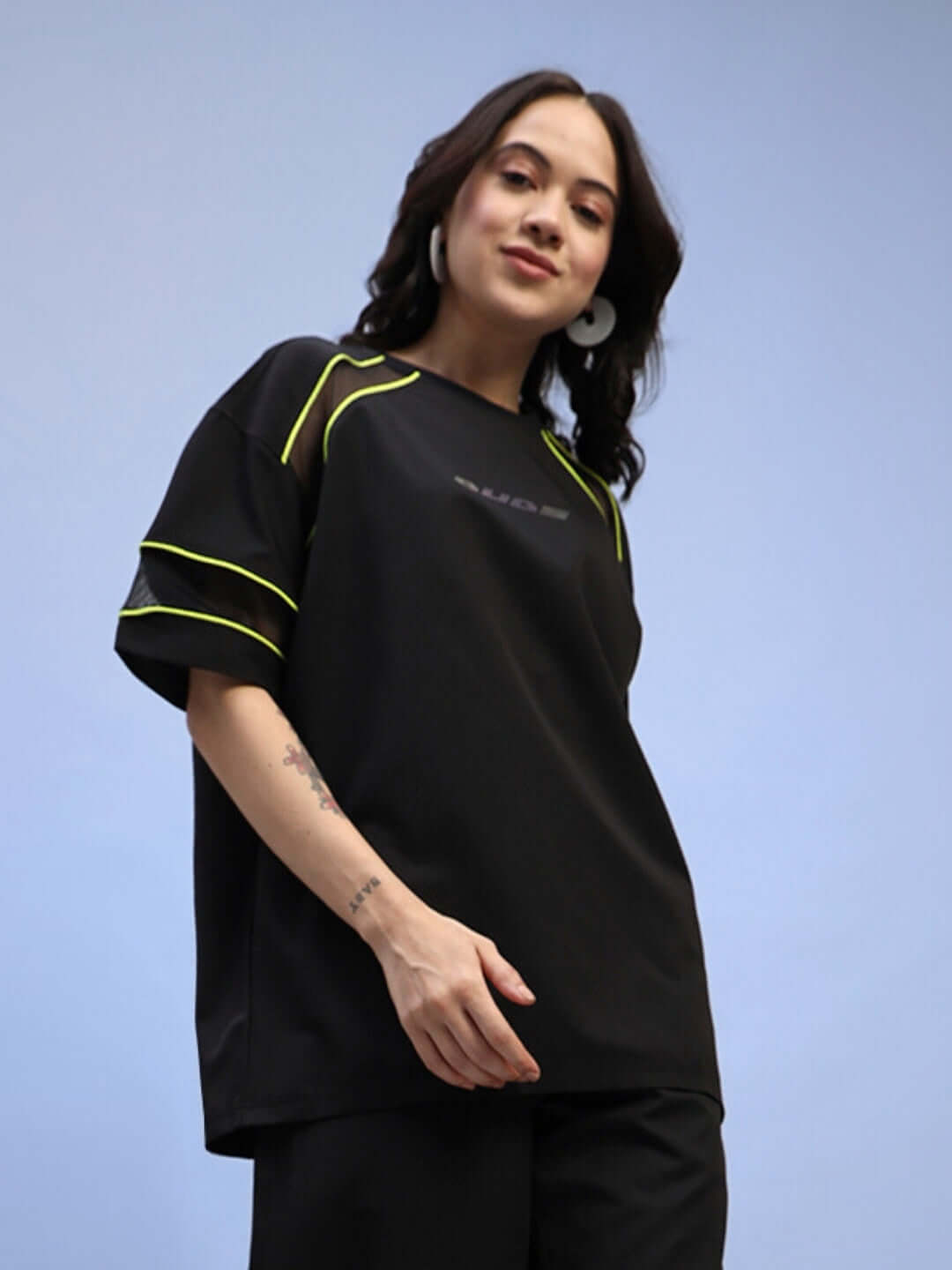 Woman wearing black women's Salvo regular fit T-shirt with neon trim, made of sports polyester fabric, model standing against blue background.