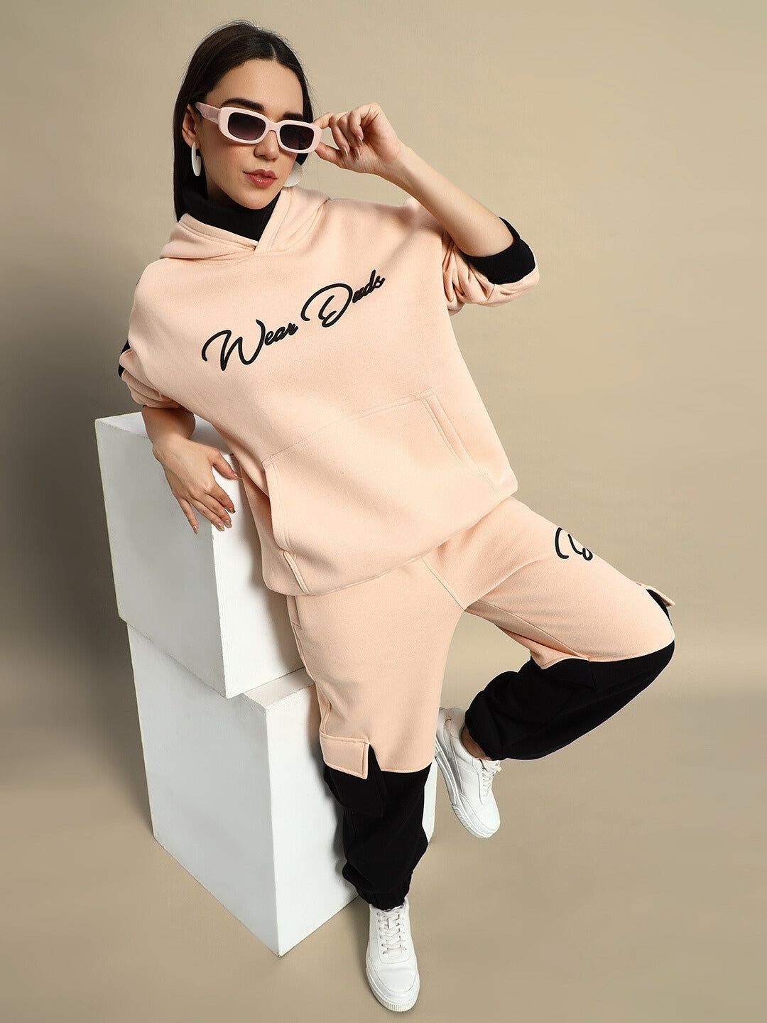 Woman wearing Women's Regiment Fleece Hoodie in beige and black, posing with sunglasses. Stylish casual wear for women.