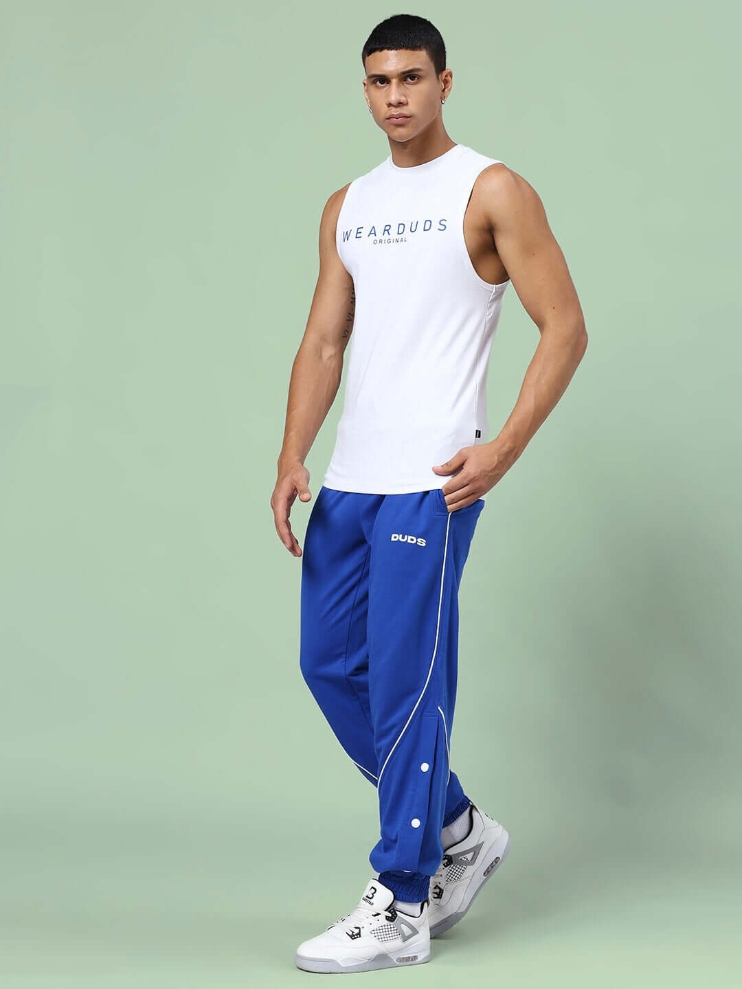 Model wearing Kickshaw Relaxed Fit Co-Ord Set in white top and royal blue joggers with elastic waistband and sneakers.