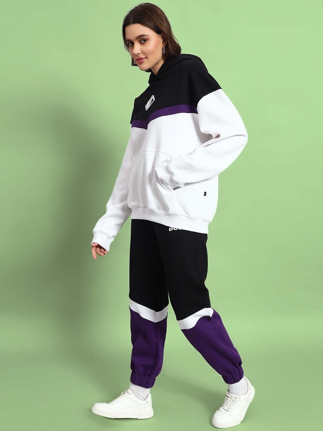 Model wearing a women's Harley fleece colorblock jogger in purple, black, and white, standing against a green background.