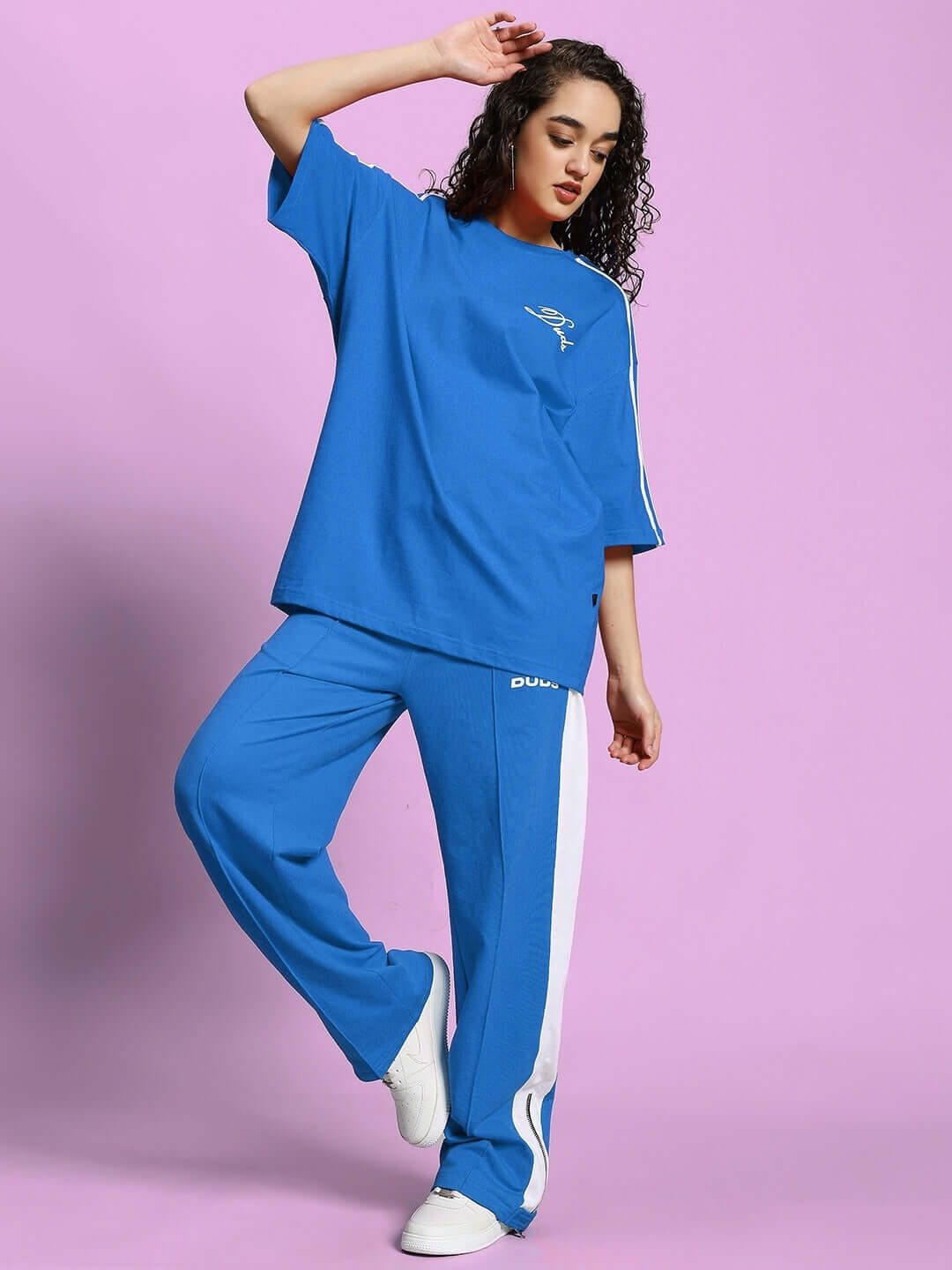 Woman wearing blue-white women's wonder slit zipper joggers and matching top against a pink background, showcasing casual fashion.