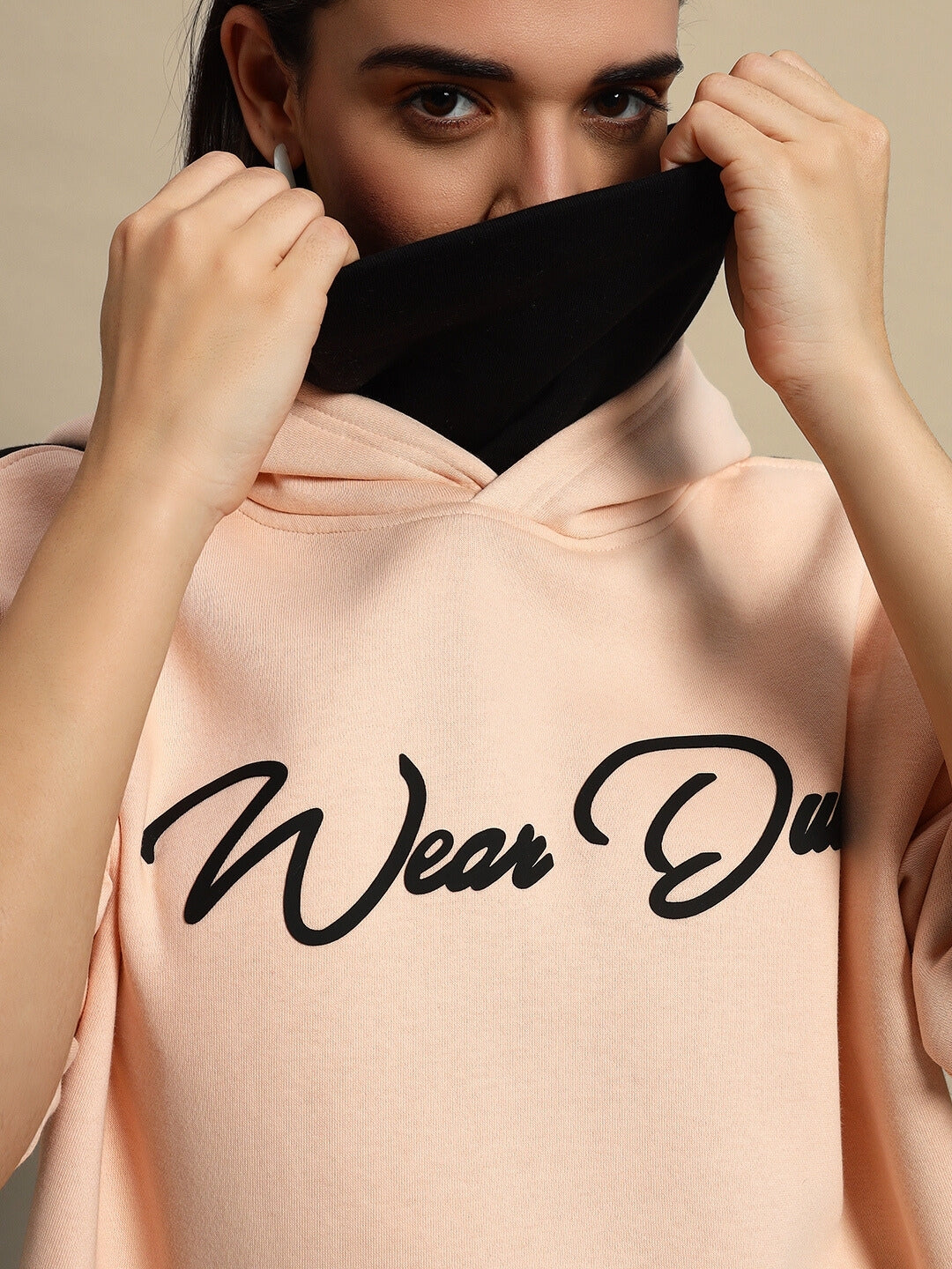 Close-up of a woman wearing a beige-black REGIMENT fleece hoodie, partially covering face, showcasing the 'Wear Du' logo on hoodie.