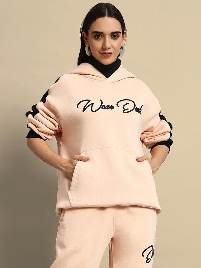 Woman wearing a beige-black fleece hoodie with 'Wear Dude' text, showcasing a stylish and comfortable fashion choice.