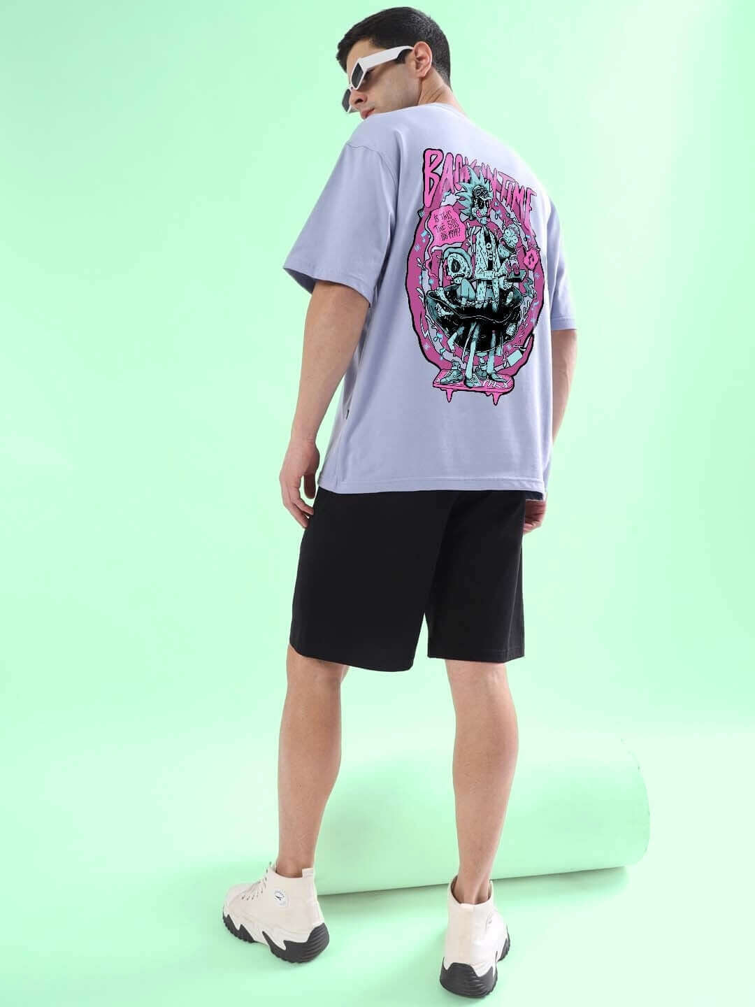 Model wearing BACK IN TIME OVER-SIZED T-SHIRT LILAC with graphic design, paired with black shorts and white sneakers, side view.