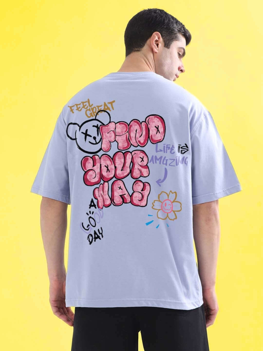 Person wearing FIND YOUR WAY OVER-SIZED T-SHIRT LILAC with graphic design on back, against yellow background.