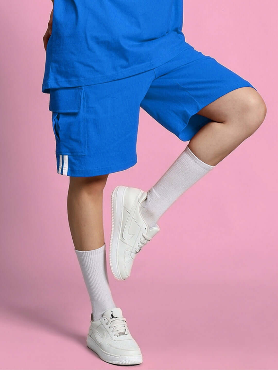 Women's Scotia Regular Fit Shorts in vibrant royal blue, paired with white sneakers and socks, against a pink background.