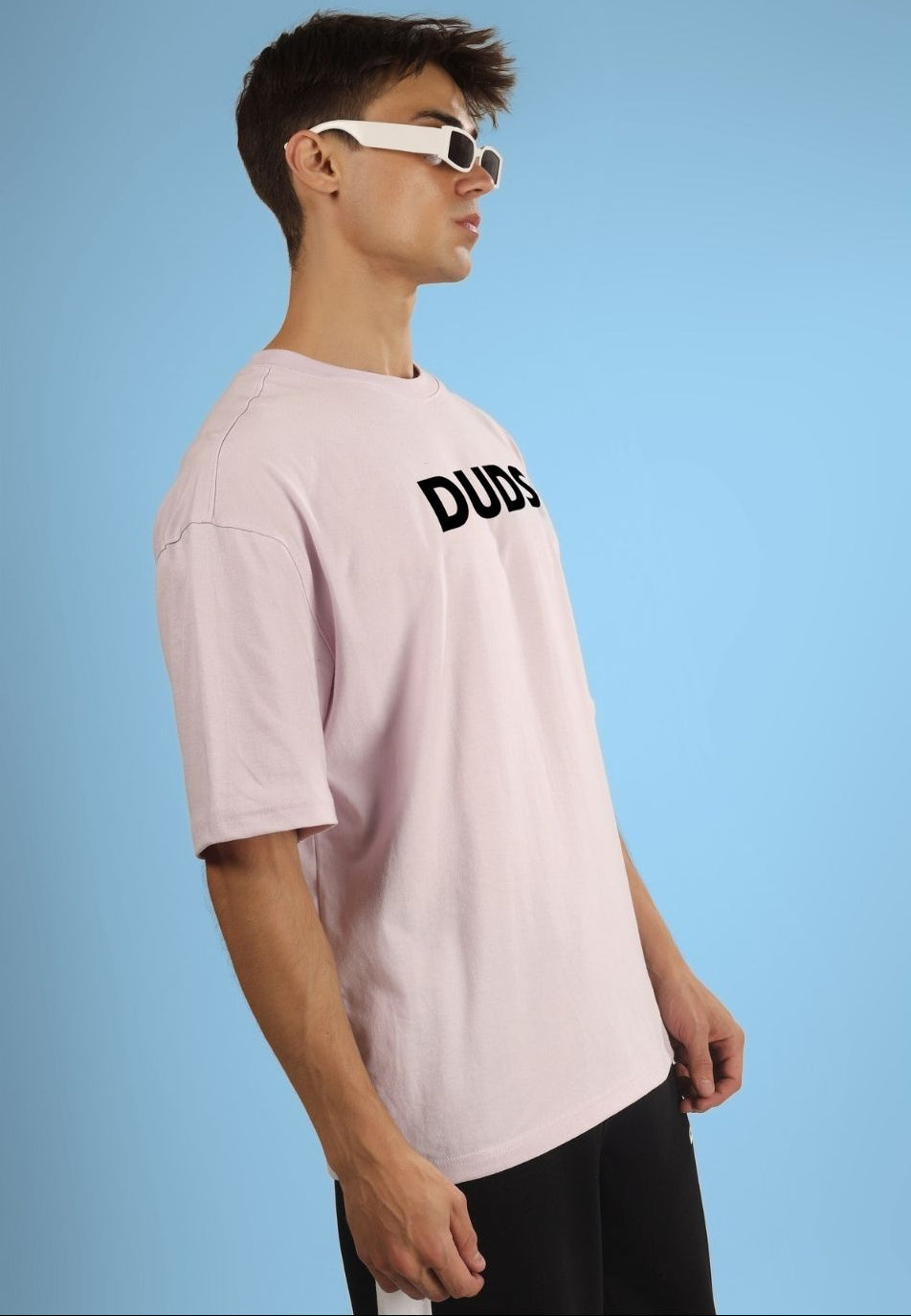 Model wearing a pastel pink oversized t-shirt with 'DUDS' lettering, standing against a blue background.