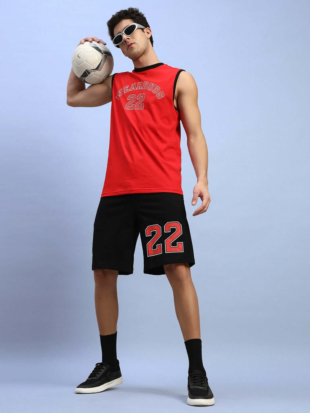 Man wearing Amiga regular fit black shorts, red sleeveless shirt, holding ball; part of customizable sportswear set.