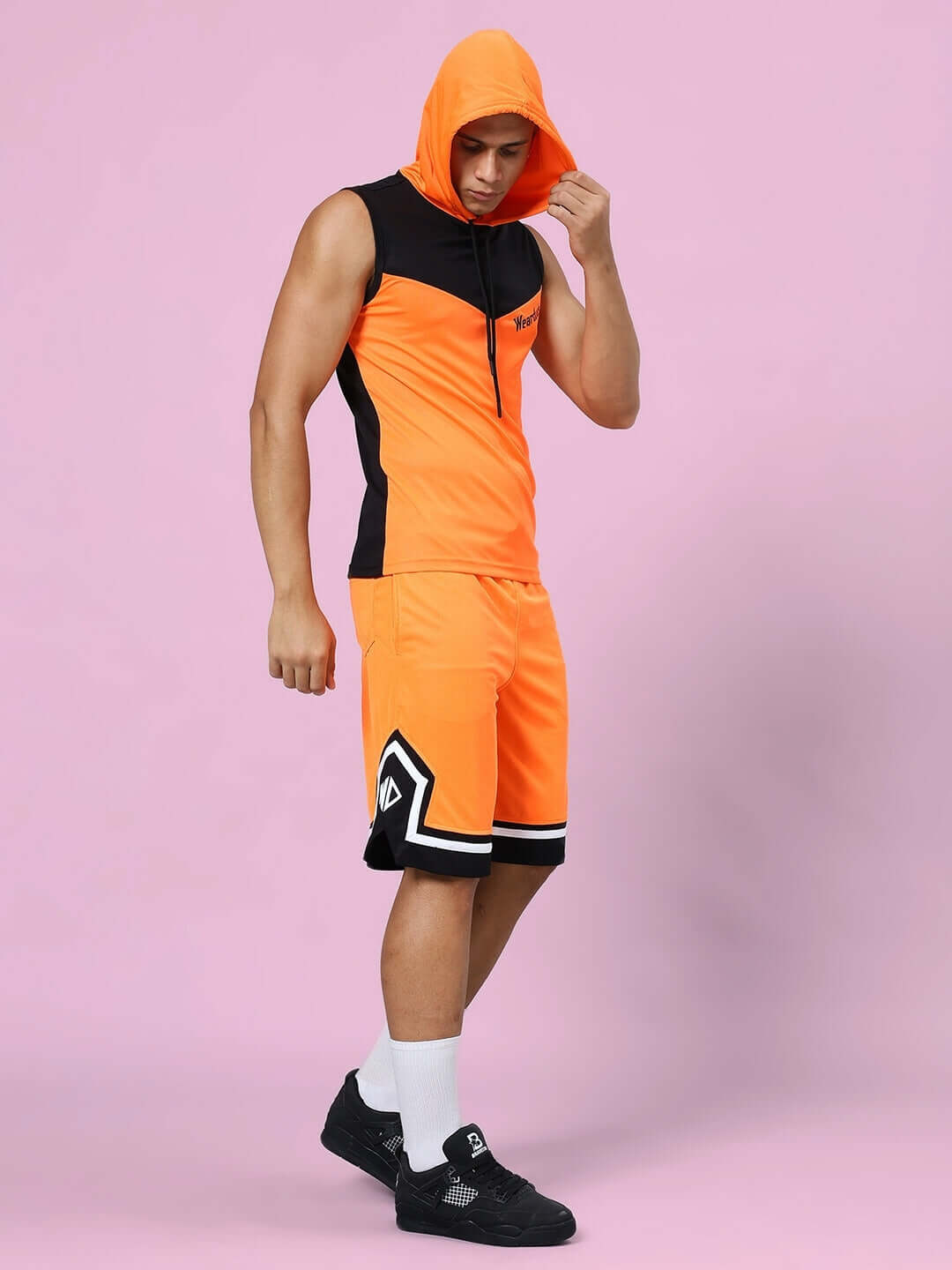 Model wearing Franky Gym Co-ord Set in orange and black, made of sports polyester, featuring a sleeveless hooded top and matching shorts.