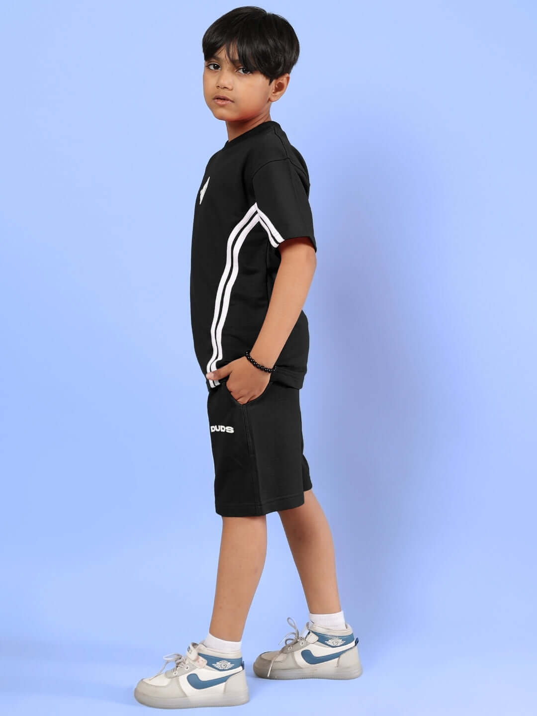 Young model wearing black Outlook half co-ord for boys and girls, made-to-order by DUDS, standing on a blue background.