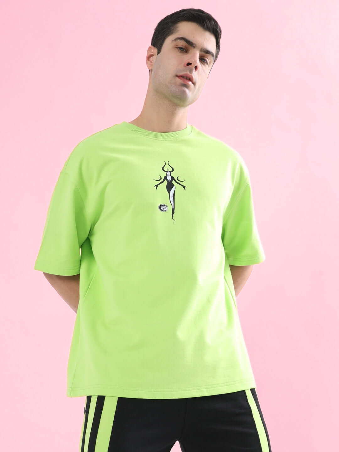 Model wearing BLACK MOON OVER-SIZED T-SHIRT NEON GREEN with moon graphic, stylish streetwear by WEAR DUDS, on pink background.