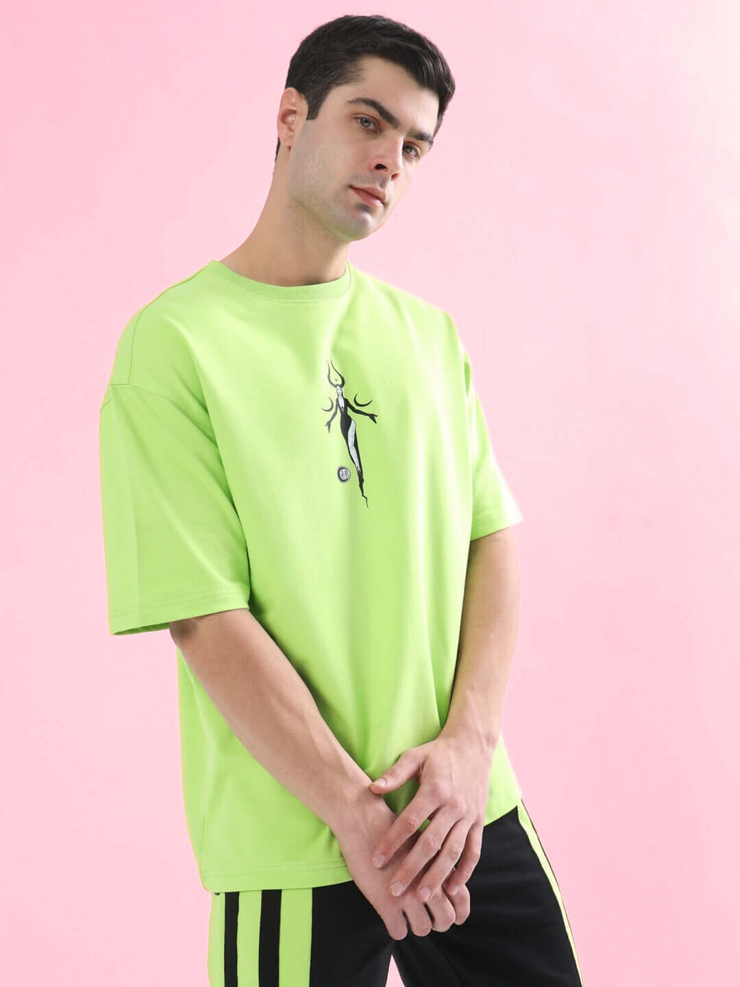 Man wearing BLACK MOON OVER-SIZED T-SHIRT NEON GREEN from WEAR DUDS against a pink background.