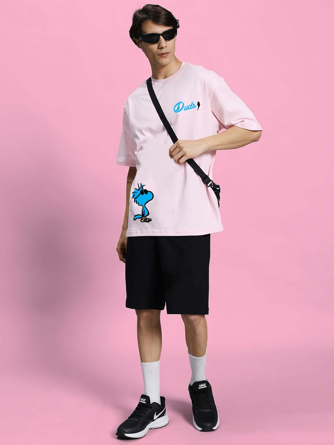 Model wearing COOL PALS regular fit black shorts paired with a pink graphic tee, showcasing casual style against a pink background.